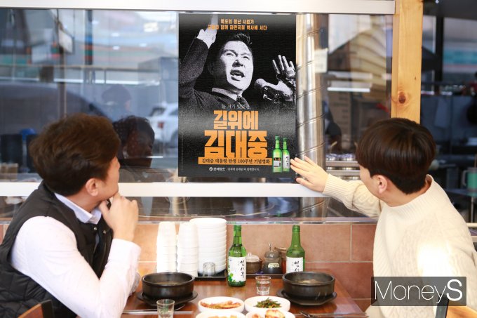 목포지역의 한 음식점에서 김대중 전 대통령 탄생 100주년을 개봉한 영화 '길위에 김대중'포스터를 손님들이 쳐다보고 있다/사진=보해양조 제공.