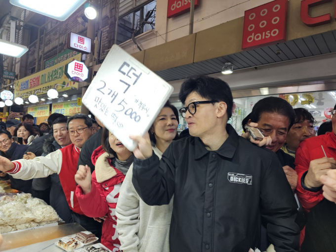 한동훈 위원장이 구리전통시장을 방문해 떡을 판매하는 상점에 들려 떡 가격이 적힌 푯말을 들어 올리며 상인과 대화를 하고 있다. /사진=이건구 기자