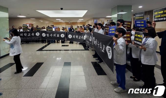 강원대학교 의과대학 교수, 전공의, 학생 40여 명이 27일 춘천 강원대병원 암센터 입구에서 이주호 교육부 장관의 현장간담회 시간에 맞춰 의과대학 정원 증원에 반대하는 피켓 들고 침묵시위를 벌였다. 이들은 검정색 마스크와 근조 리본을 달고 있었다.2024.3.27(독자 제공) ⓒ News1 한귀섭 기자