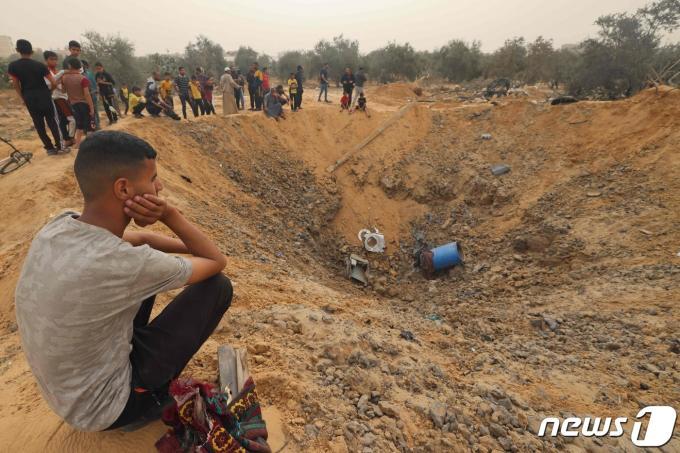 가자 남부 라파 주민들이 18일 밤 사이 지속된 이스라엘군 포격에 움푹 파인 폭탄 웅덩이를 멍하니 바라보고 있다. 2024.04.18 ⓒ AFP=뉴스1 ⓒ News1 김성식기자