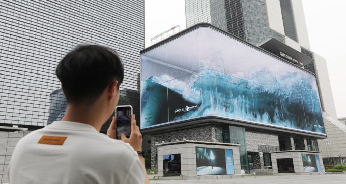 서울 강남구 코엑스 앞을 지나던 시민이 전광판에서 몰아치는 입체 파도 'Wave'를 스마트폰에 담고 있다. /사진=뉴스1
