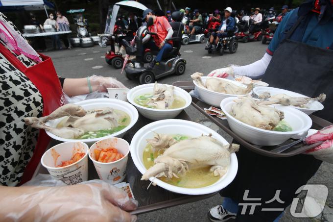 삼복더위의 시작을 알리는 초복을 나흘 앞둔 11일 대구 달서구 두류공원 사랑해밥차 무료급식소에서 자원봉사자들이 몸이 불편한 어르신께 삼계탕을 전달하고 있다. 이날 사랑해밥차는 초복을 앞두고 복달임으로 1300마리 닭으로 삼계탕을 끓이고 수박 30통을 후식으로 준비했다. 2024.7.11/뉴스1 ⓒ News1 공정식 기자