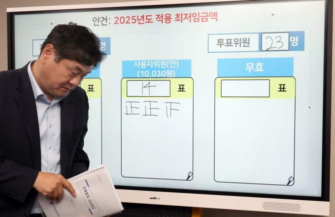 이인재 최저임금위원장이 지난 12일 새벽 세종시 정부세종청사에서 2025년도 적용 최저임금이 1만30원으로 결정된 직후 표결 결과가 표시된 화면 앞을 지나고 있다. / 사진=뉴시스 강종민 기자 