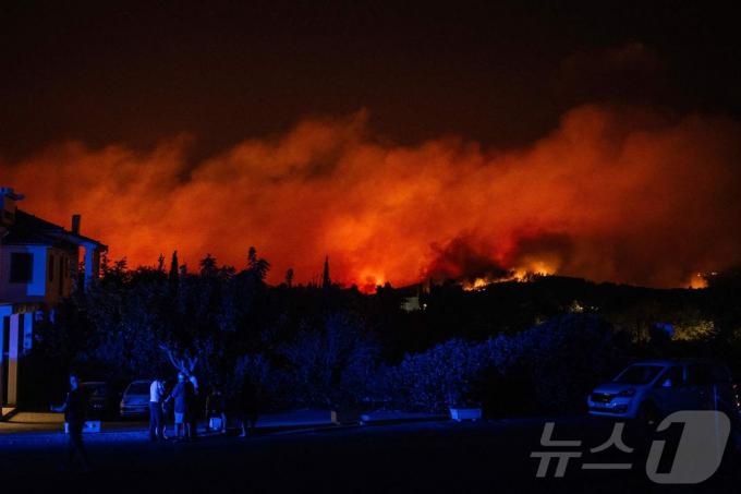 11일(현지시간) 아테네 북쪽 바르나바스의 한 산비탈에서 산불이 타오르고 있는 가운데 지역 주민들이 길을 따라 서 있다. 24.08.11 ⓒ AFP=뉴스1 ⓒ News1 김예슬 기자