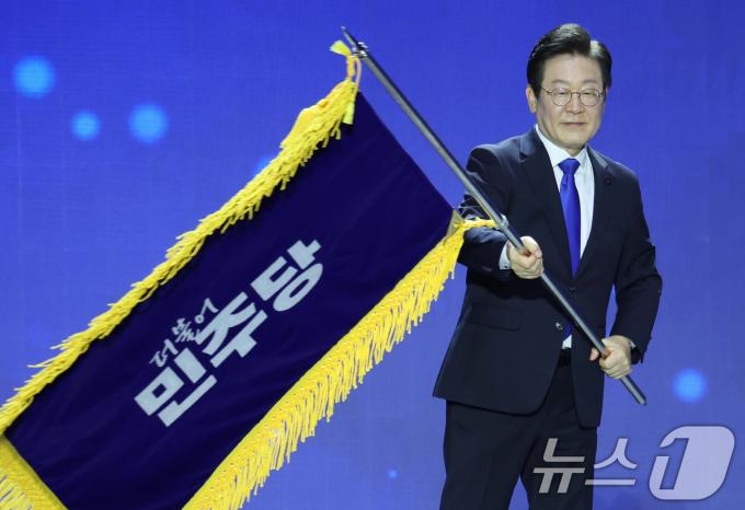 연임에 성공한 이재명 더불어민주당 대표가 18일 서울 송파구 올림픽공원 KSPO돔에서 열린 제1차 전국당원대회에서 당기를 흔들고 있다. (공동취재)2024.8.18/뉴스1 ⓒ News1 김민지 기자