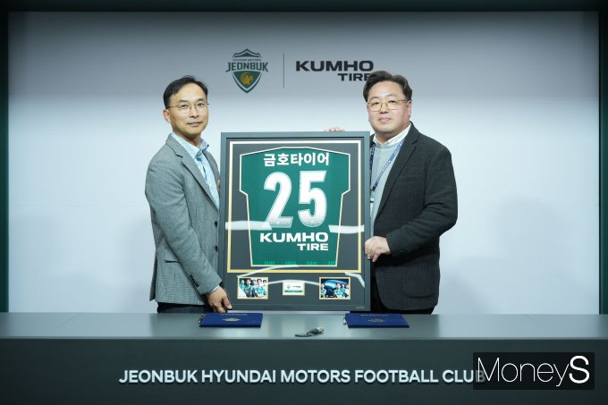 윤민석 금호타이어 G.마케팅담당 상무(왼쪽)와 이도현 전북현대모터스  단장이 공식 파트너십 연장  조인식을 체결하며 금호타이어 로고가 적용된 유니폼 액자를 들고 기념사진을 찍고 있다/사진=금호타이어 제공.
