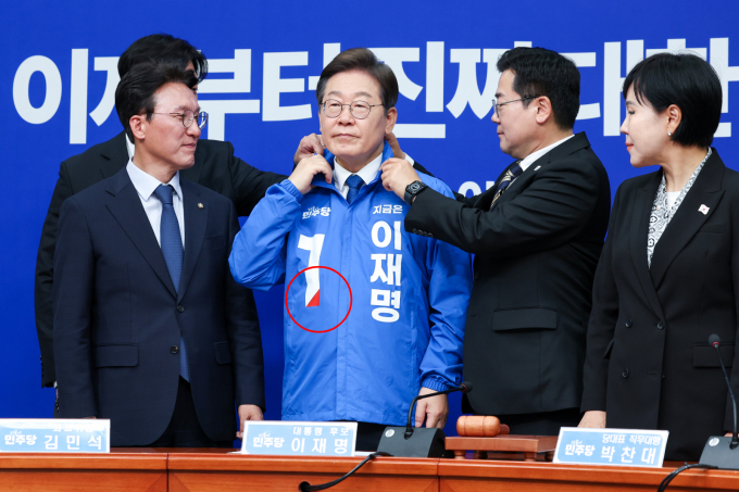 이재명 더불어민주당 대선 후보가 빨간색 점이 찍힌 선거 점퍼를 입어 눈길을 끄는데 보수를 상징하는 빨간색을 사용함으로써 통합 의지를 담아냈다는 분석이다.  사진은 지난 28일 박찬대 더불어민주당 대표 직무대행 겸 원내대표(오른쪽에서 두번째)가 서울 여의도 국회에서 열린 최고위원회의에서 이재명 대선 후보(파란색 점퍼)에게 선거복을 입혀준 뒤 옷깃을 정리하고 있는 모습. /사진=뉴스1