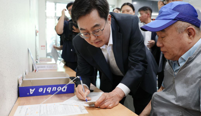 김동연 경기도지사가 민생회복 소비쿠폰 지급신청 첫날인 21일 수원시 원천동 행정복지센터를 방문, 서류 작성이 서툰 한 어르신을 돕고 있다. /사진제공=경기도